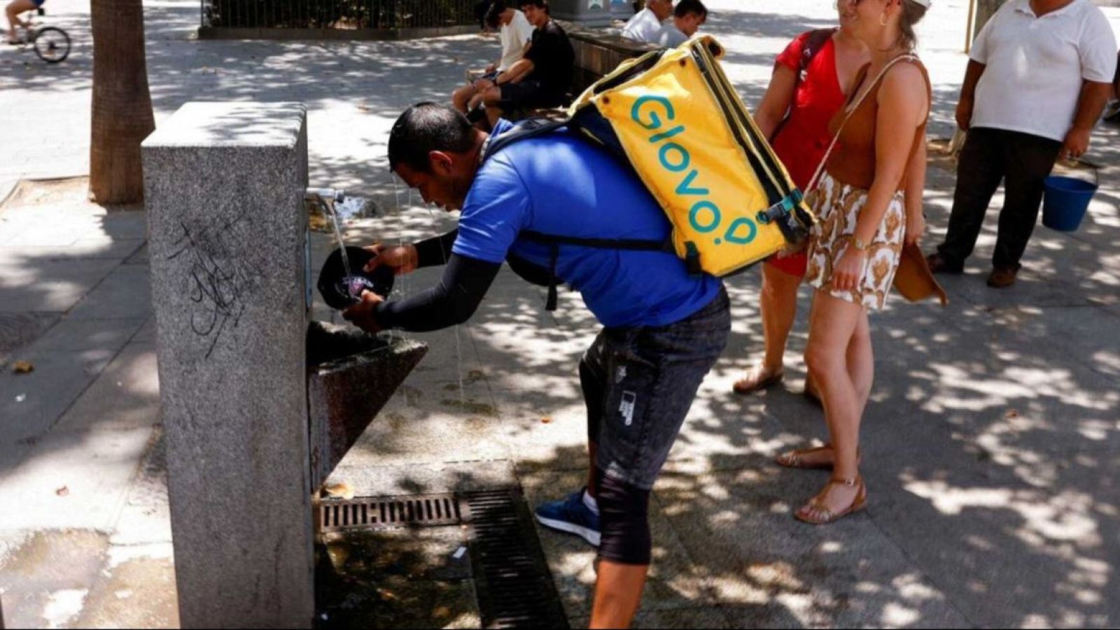 Un home mulla la gorra a l'aigua d'una font per refrescar-se.