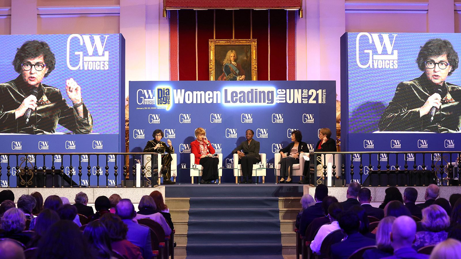 Un evento en Madrid, "GW Voices", muestra a cinco mujeres oradoras en un escenario con un telón de fondo azul y el logo "GW". La audiencia observa a las oradoras y las pantallas laterales con el logo del evento.