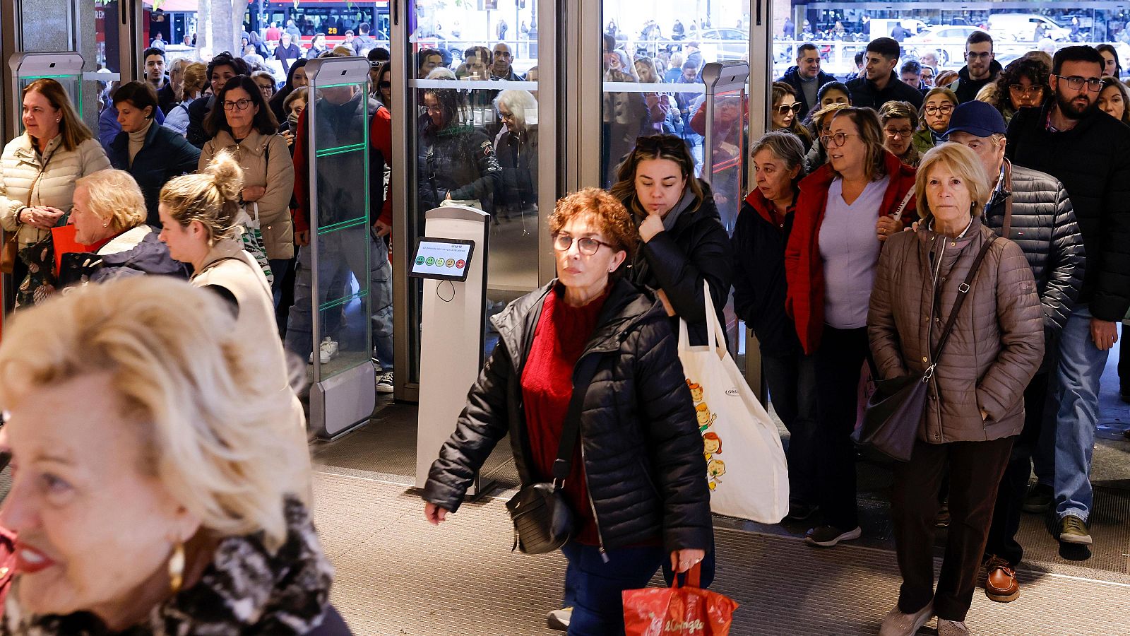 Una gran cantidad de personas, vestidas con ropa de abrigo, se dirigen a la entrada de una tienda, posiblemente atraídas por las rebajas. Algunos ya llevan bolsas de compras, anticipando la adquisición de productos.