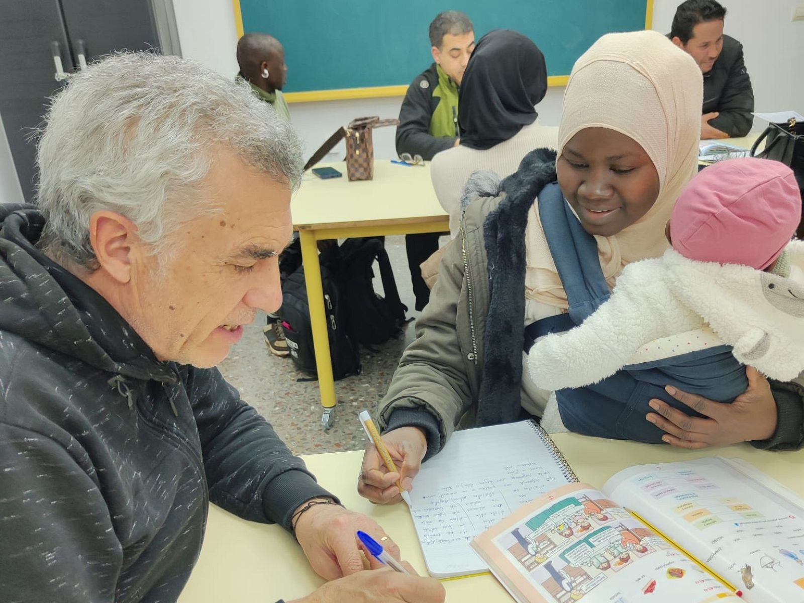En la imagen aparece una mujer de origen marroquí escribiendo en un cuaderno junto a su profesor-
