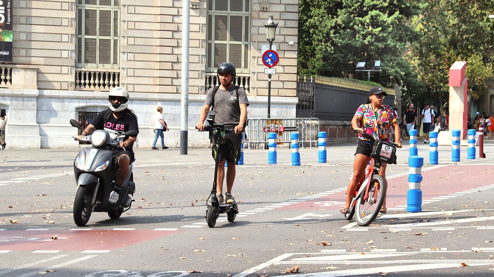 Una moto, un patinet i una bici circulen per un carrer de Barcelona