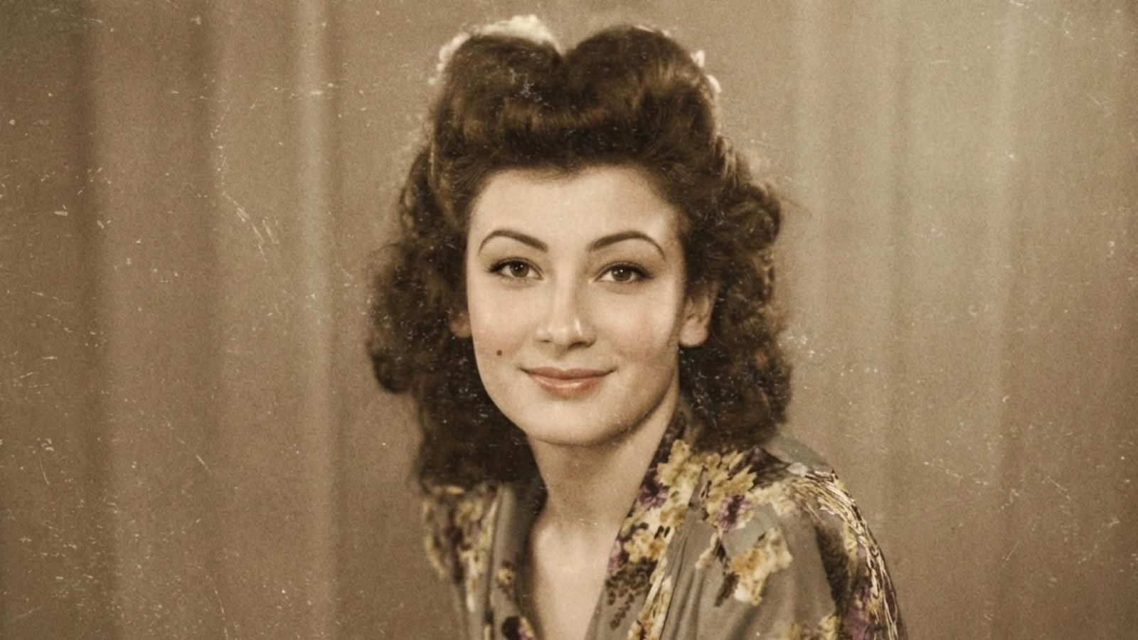 Retrato en tonos sepia de una mujer con cabello castaño oscuro peinado con ondas y un recogido, luciendo una prenda con estampado floral. Se observa un lunar en su mejilla izquierda.