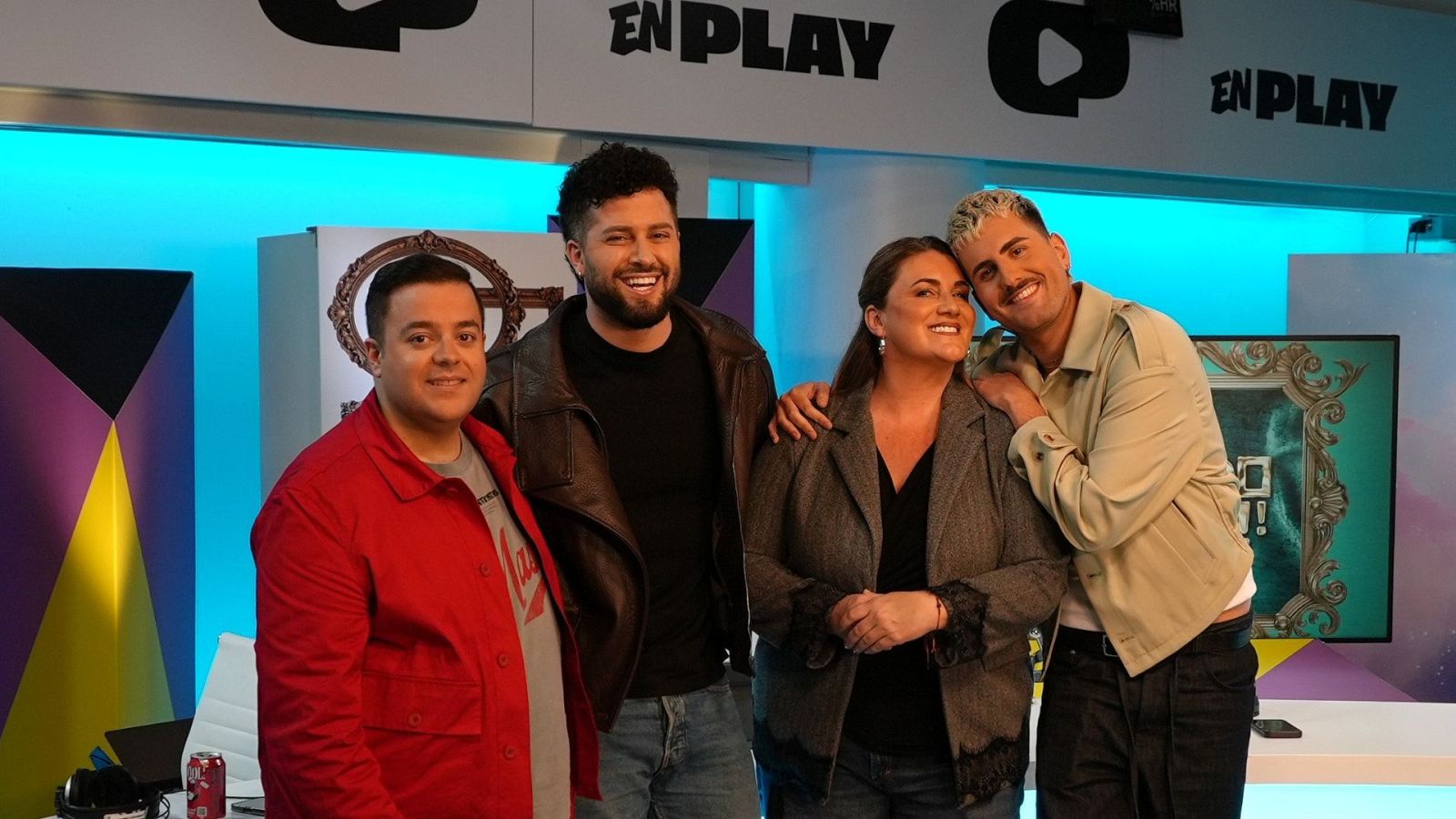 Cuatro personas sonríen en un estudio de radio, posando para una foto. Entre ellos, un hombre con chaqueta de cuero y camiseta negra, junto a otros tres individuos, frente a un letrero "EN PLAY".