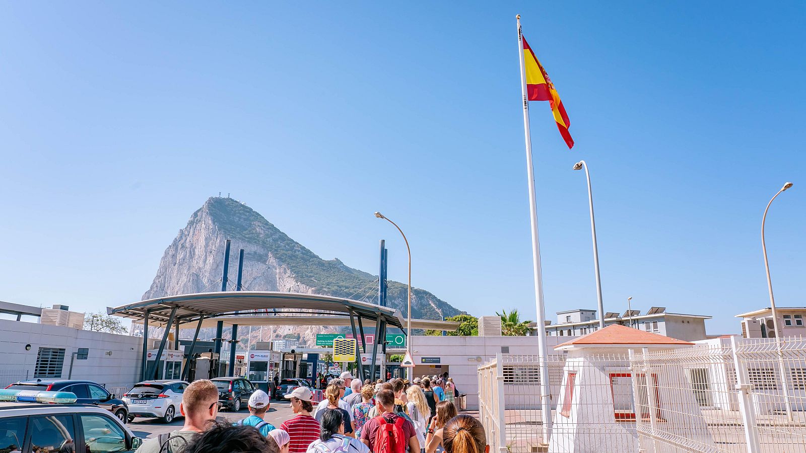 Vista de la frontera de Gibraltar con el Peñón al fondo y una bandera de España en primer plano, representando el nuevo tratado de libre circulación