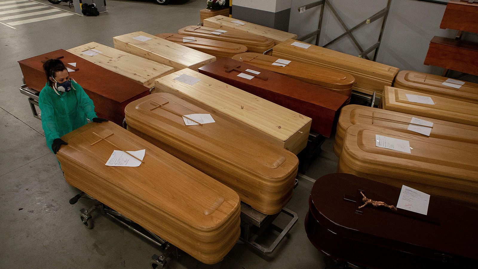 Una trabajadora de servicios funerarios organiza una hilera de féretros de madera almacenados en una nave industrial de grandes dimensiones