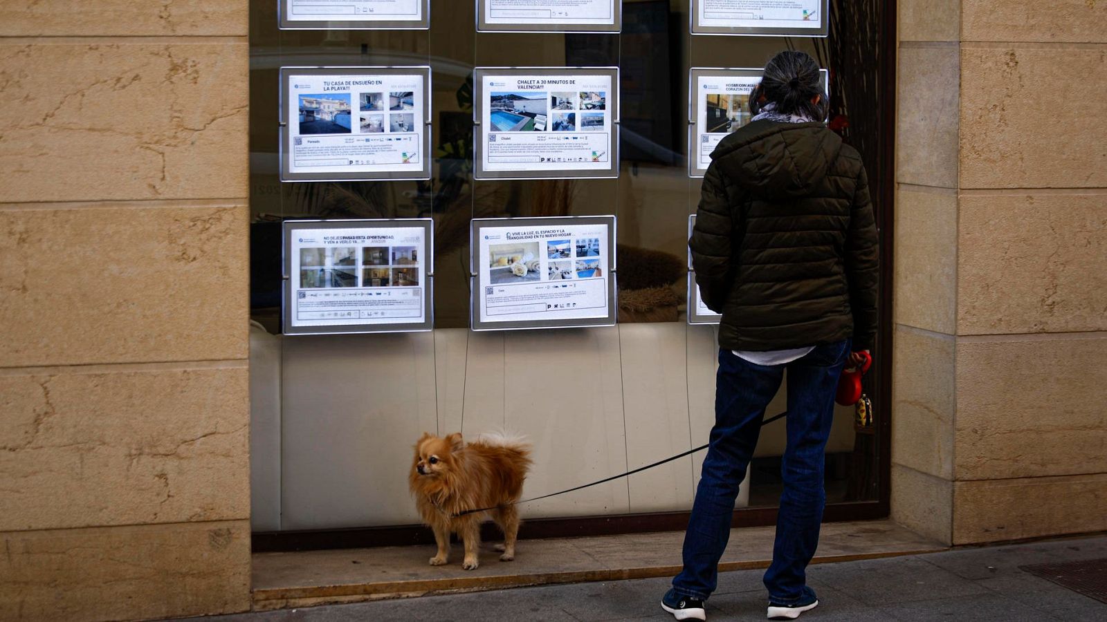 En la imagen aparece un hombre acompañado de su perro frente al escaparate de una agencia inmobiliaria