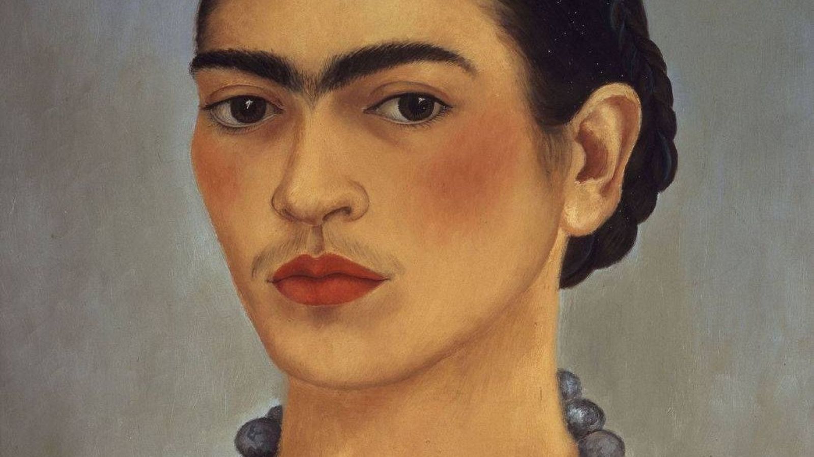 En el autorretrato de 1933, una mujer con cejas prominentes y labios rojos se presenta con un collar oscuro y trenzas en el cabello.