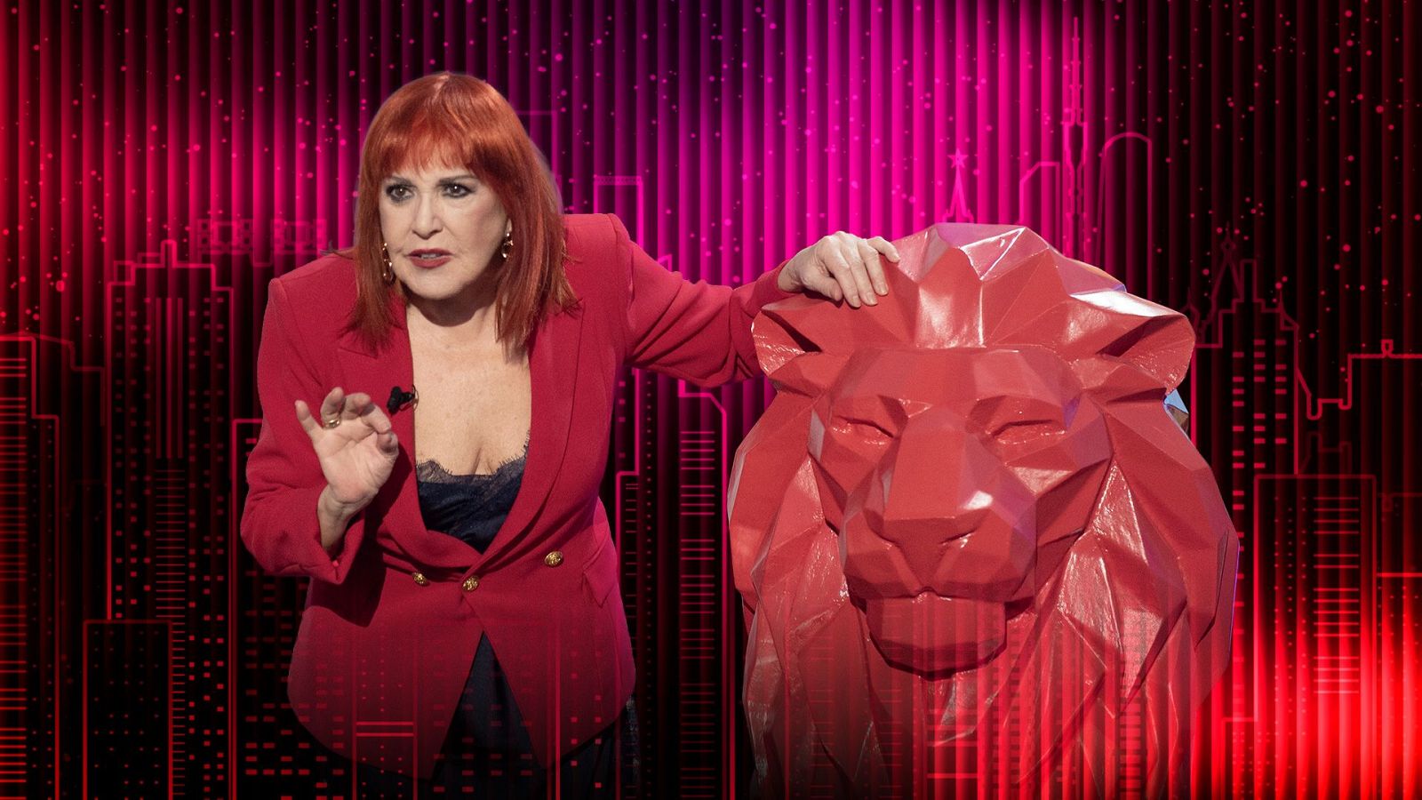 Loles León, con chaqueta roja y blusa oscura, gesticula junto a una escultura de león rojo sobre un fondo abstracto en tonos rojos y negros, con el texto "Zero dramas" en la parte superior.