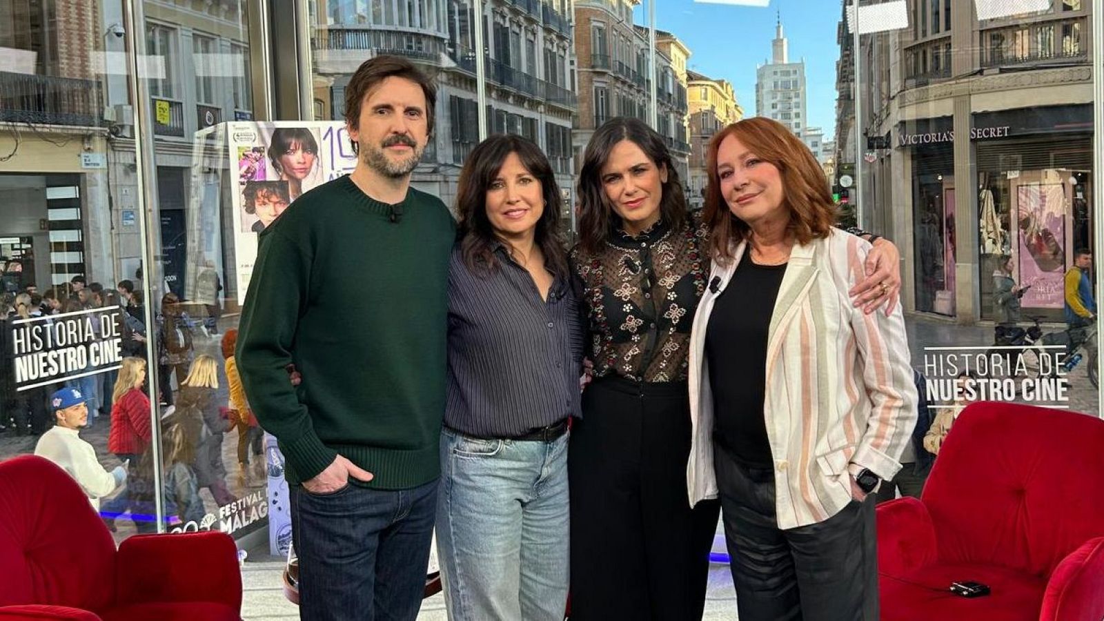 Cuatro personas posan frente a un fondo que simula una calle. Se distinguen un hombre con jersey verde, una mujer con camisa a rayas, otra con blusa negra y una cuarta con chaqueta a rayas.