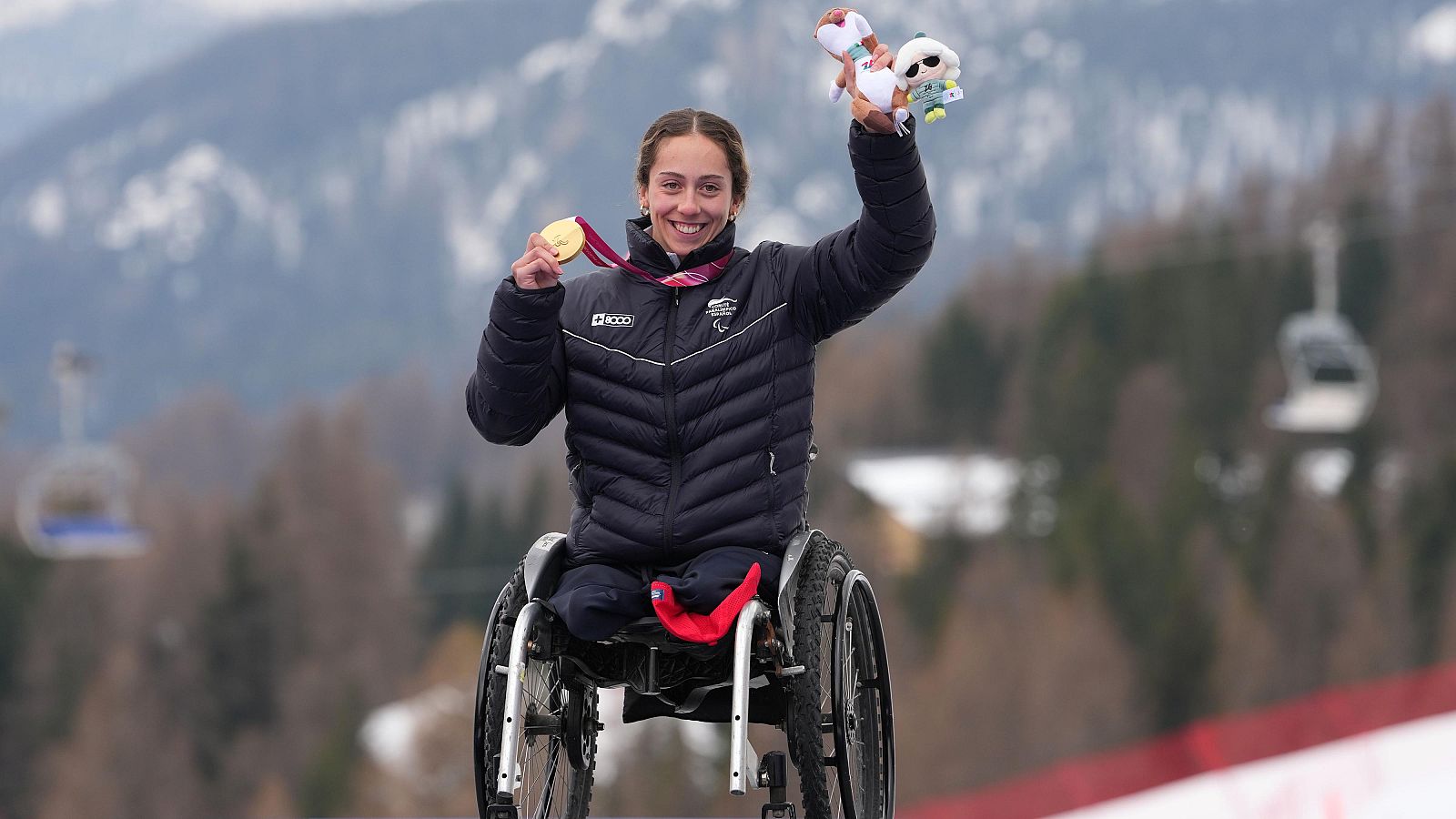 La esquiadora paralímpica Audrey Pascual sonríe sentada en su silla de esquí mientras muestra una de sus medallas ganadas en Milano Cortina 2026
