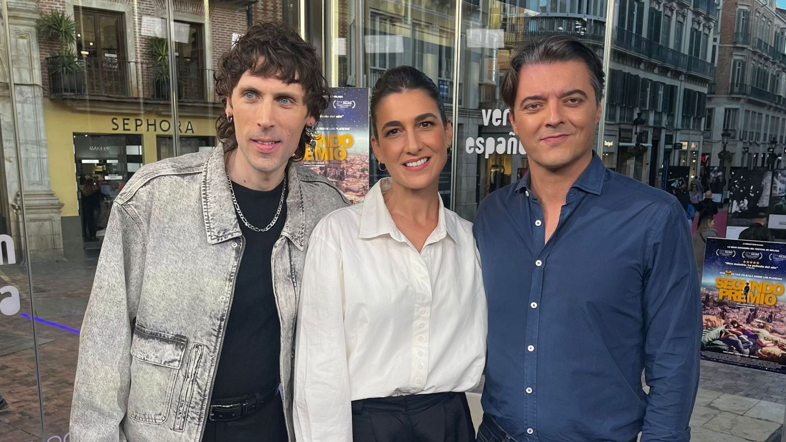 Tres individuos se presentan ante una cristalera; Cristalino con chaqueta vaquera, Stéphanie Magnin con camisa blanca y Cristóbal García Ortiz con camisa azul, con un cartel de "Segundo Premio" al fondo.