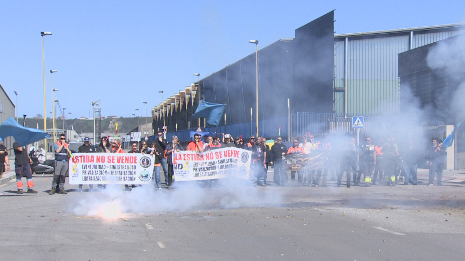 Un grupo de personas con chalecos reflectantes protestan en la calle frente a un edificio, sosteniendo pancartas con consignas contra la privatización y la eventualidad laboral, mientras el humo se eleva en el aire.