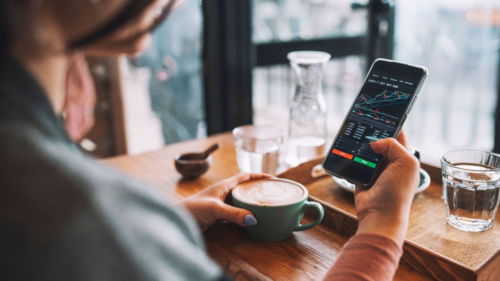 Mujer que usa un teléfono inteligente compra criptomonedas en una cafetería