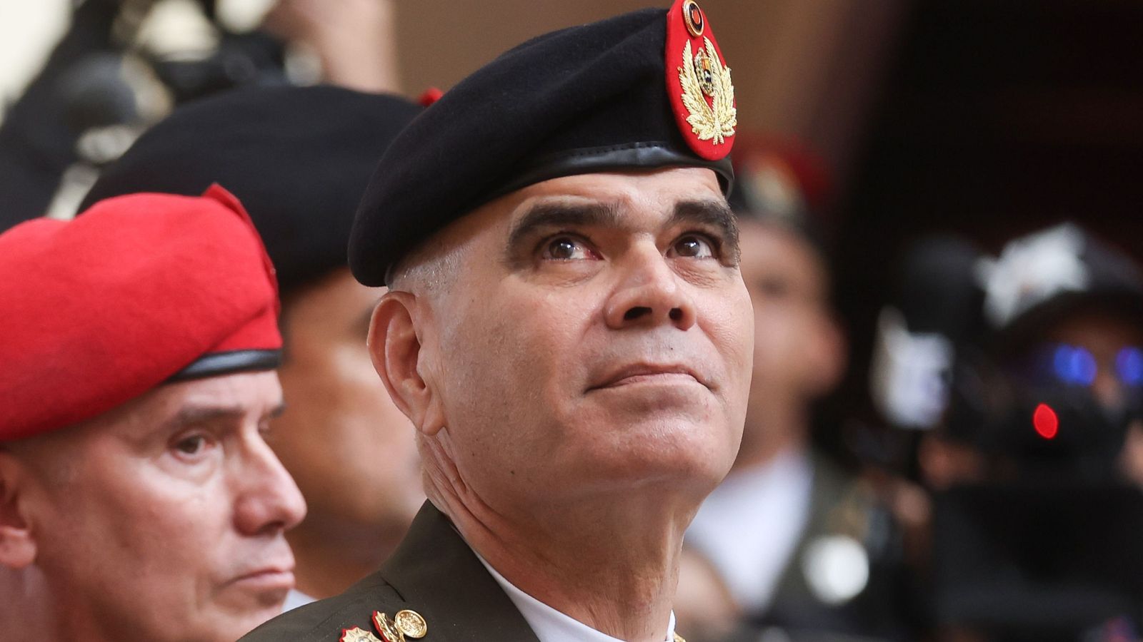 El Ministro de Defensa de Venezuela, Vladimir Padrino López, posa con uniforme militar y boina negra. La imagen sugiere un evento público, con otras personas y equipos de cámara en el fondo.