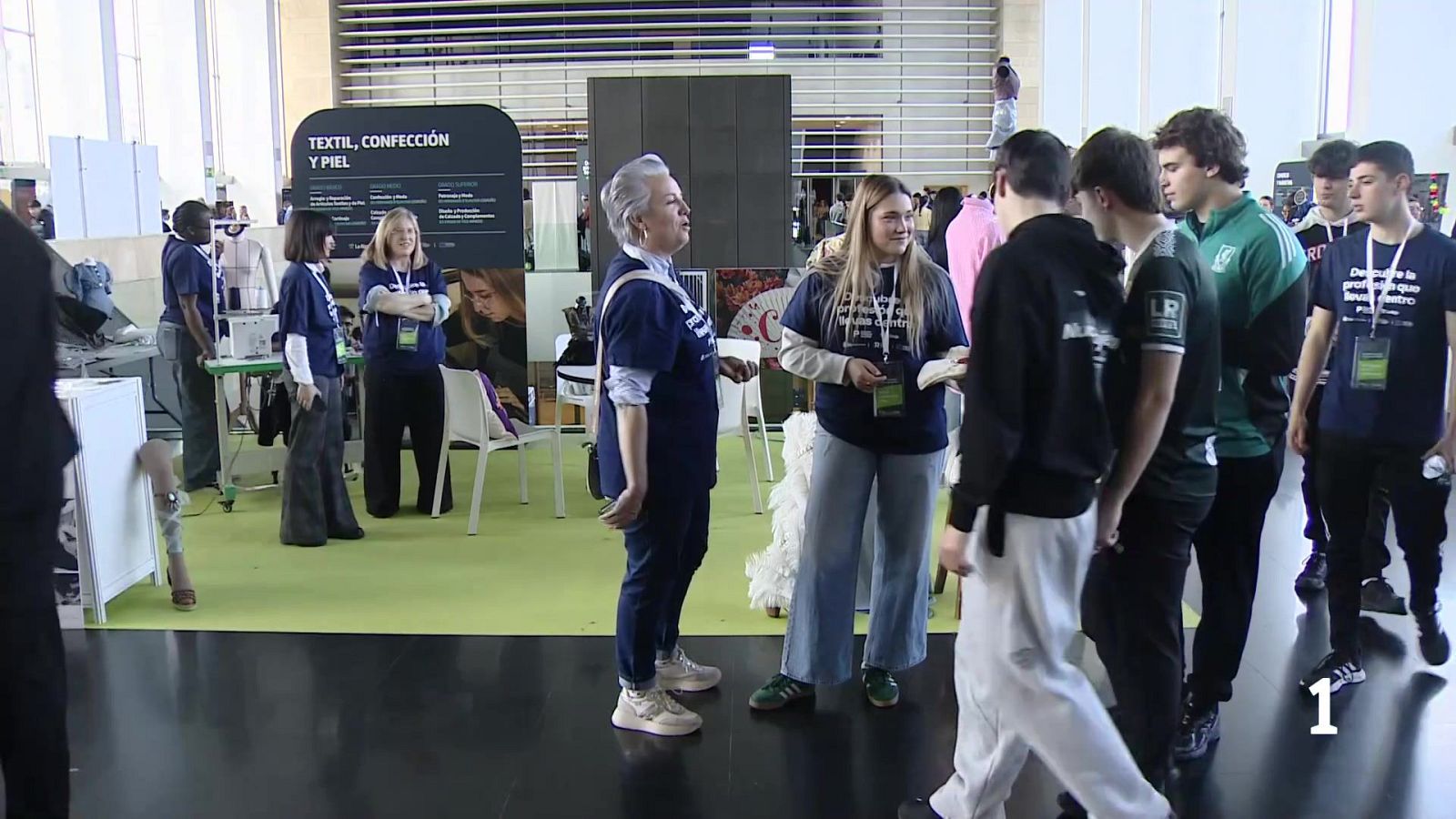 En un evento en La Rioja, un grupo de personas conversa frente a un stand que exhibe productos textiles. Se observan individuos con camisetas y elementos relacionados con la confección y la piel.