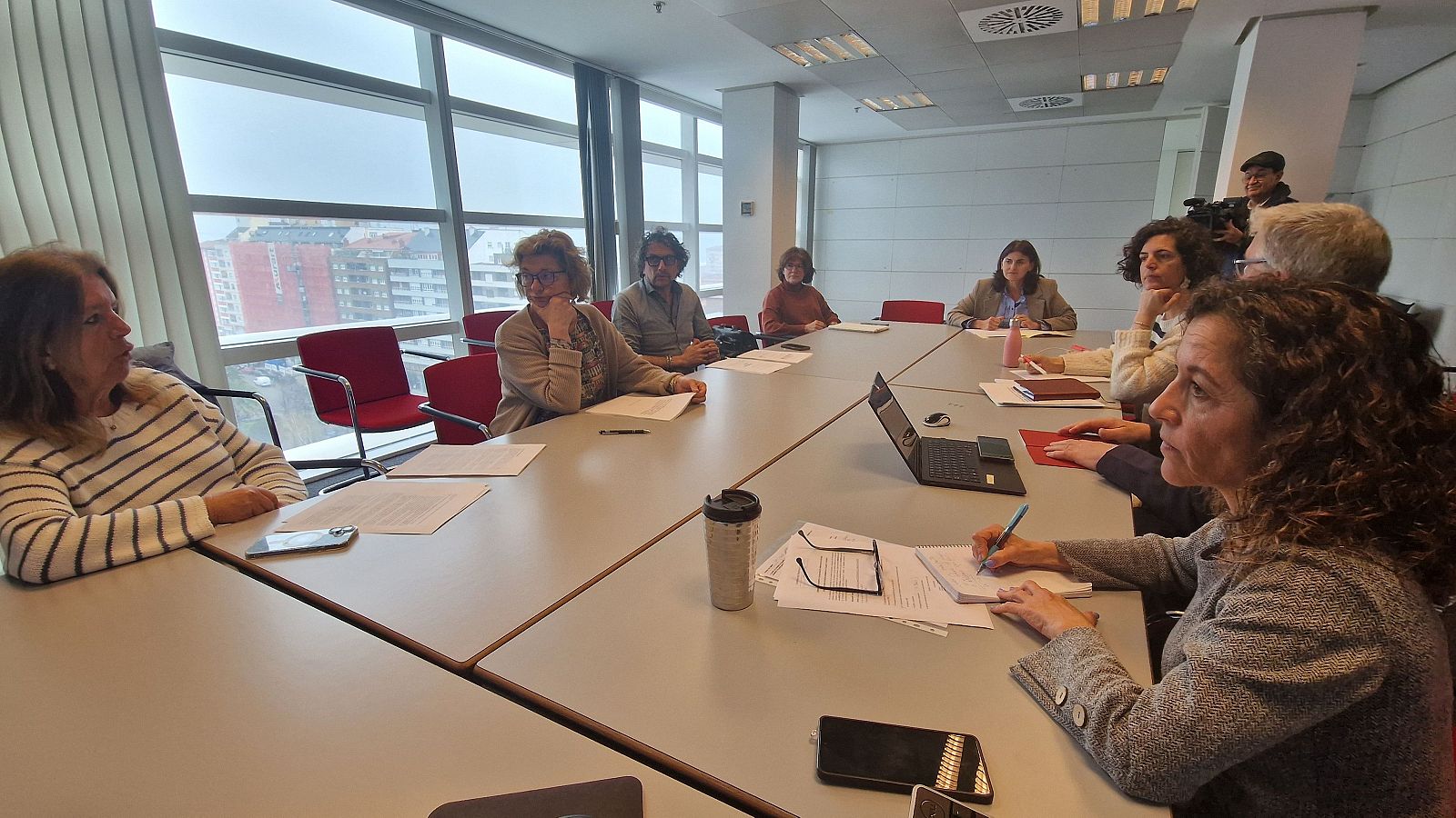 Una reunión en Asturias con varias personas alrededor de una mesa; una mujer con cabello rizado toma notas, posiblemente la Directora General de Cuidados y Coordinación Sociosanitaria, mientras que otros miran hacia ella o hacia el frente.