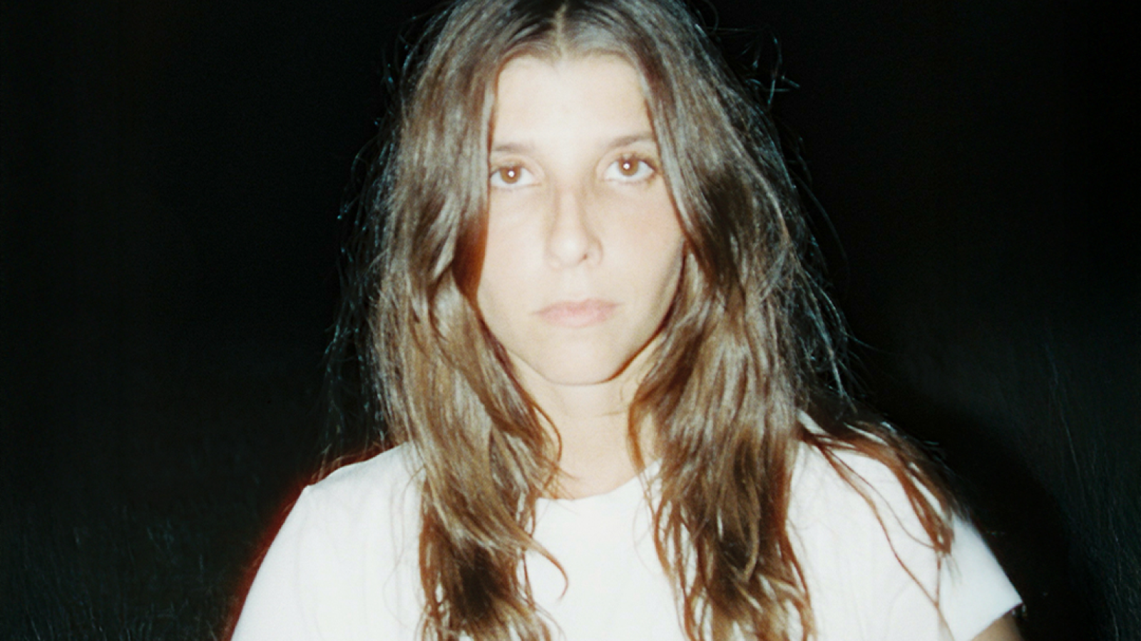 Una mujer de cabello castaño largo, con camiseta blanca y ojos marrones, posa para la cámara. Se identifica a la persona como Ona Mafalda.