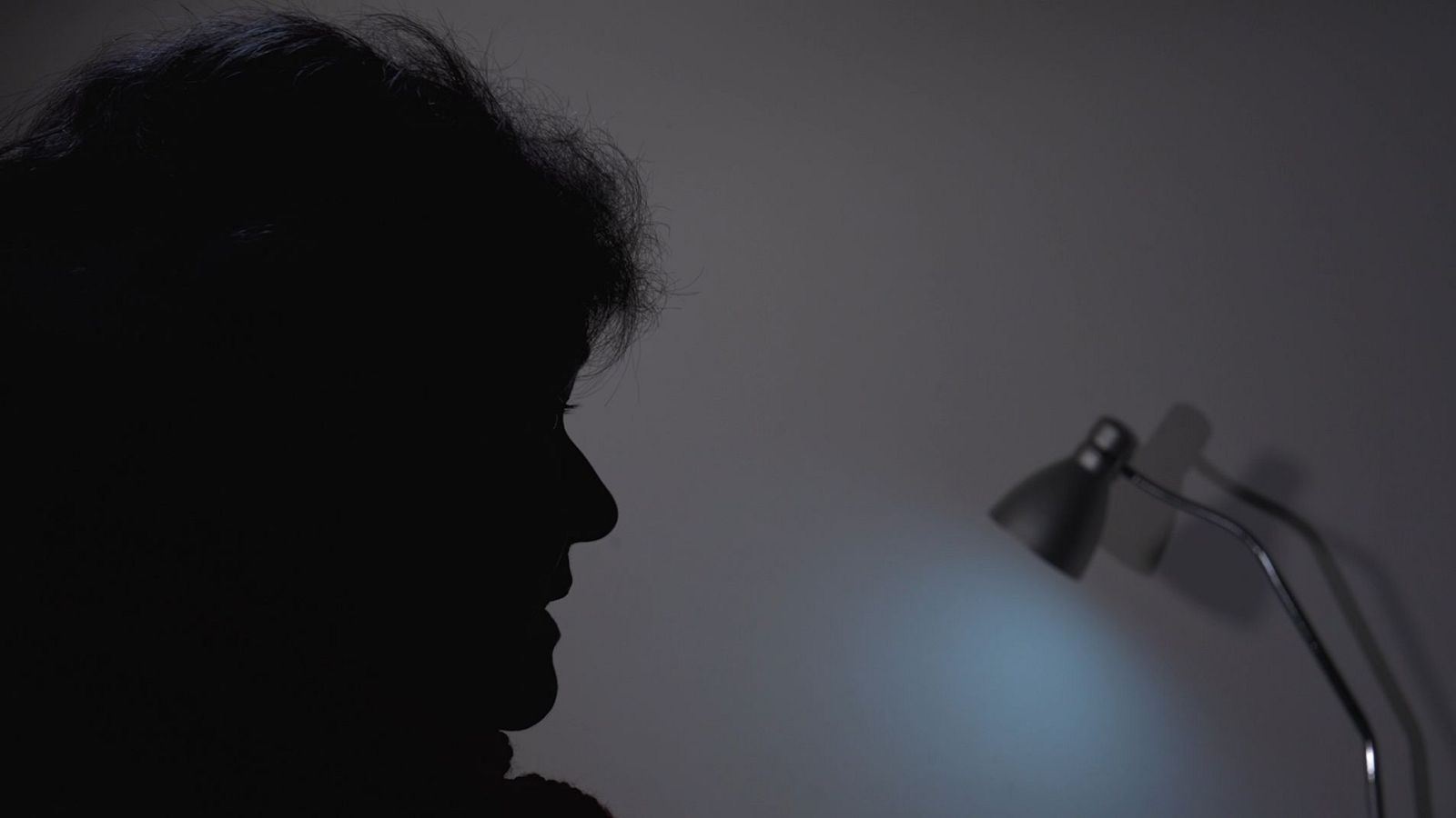 Una silueta femenina, identificada como Ruth Ortiz, se recorta contra un fondo gris. Una lámpara de escritorio ilumina el espacio con una luz azulada, generando una atmósfera introspectiva.