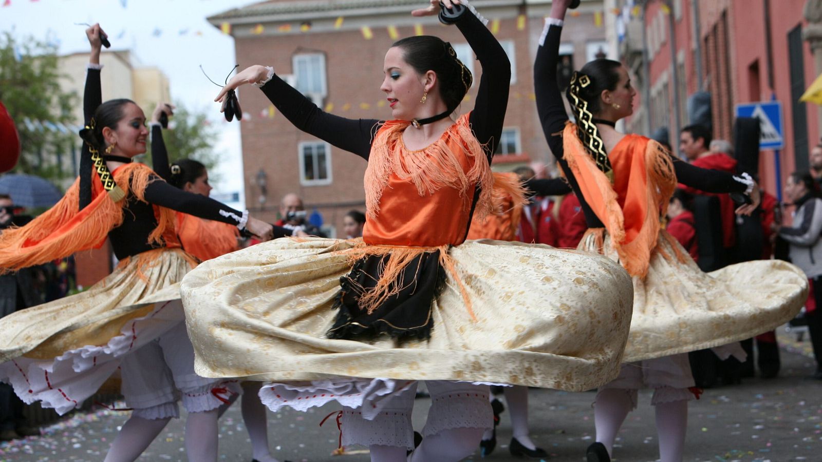 Un grupo de bailarinas, ataviadas con trajes tradicionales, ejecutan una danza en una calle. Destacan las faldas amplias, las blusas negras y los corpiños adornados, creando una atmósfera festiva.