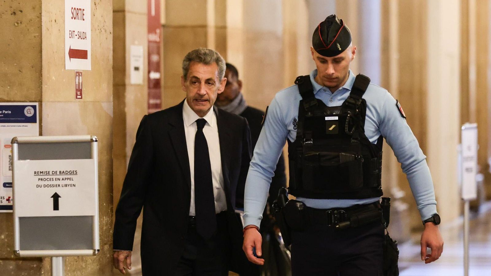 Fotografía del expresidente francés Nicolas Sarkozy acompañado de un agente de la gendarmerie entrando al tribunal el primer día de su interrogatorio