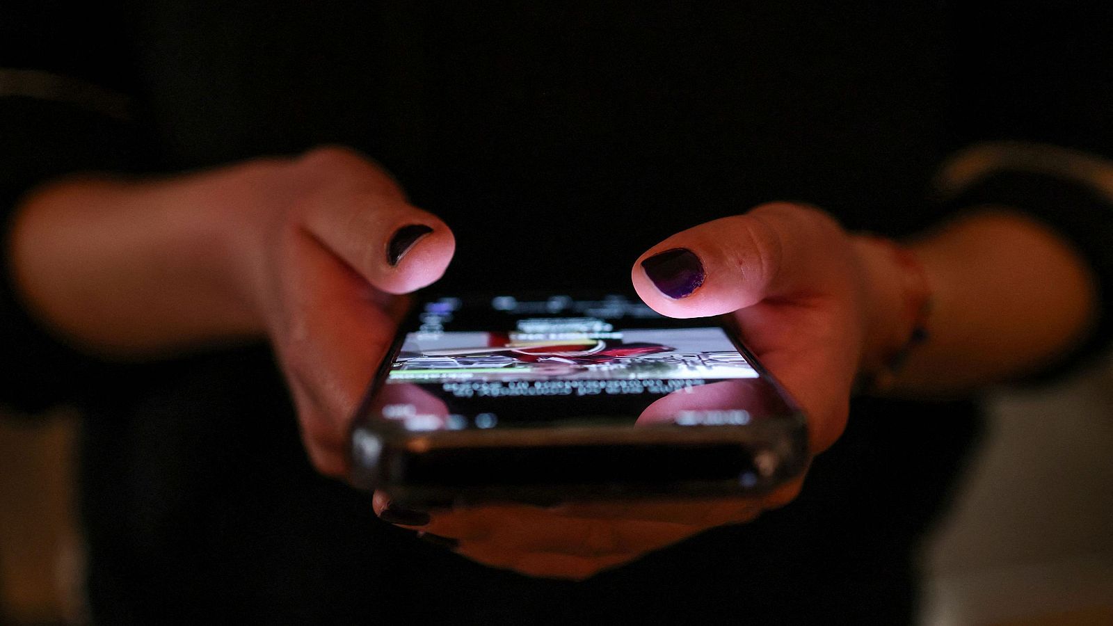 Imagen de las manos de una adolescente con un teléfono móvil, revisando las publicaciones en redes sociales
