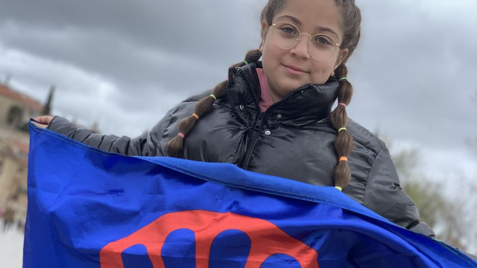 Niña sosteniendo con orgullo la bandera gitana azul y verde con la rueda roja en un acto reivindicativo.