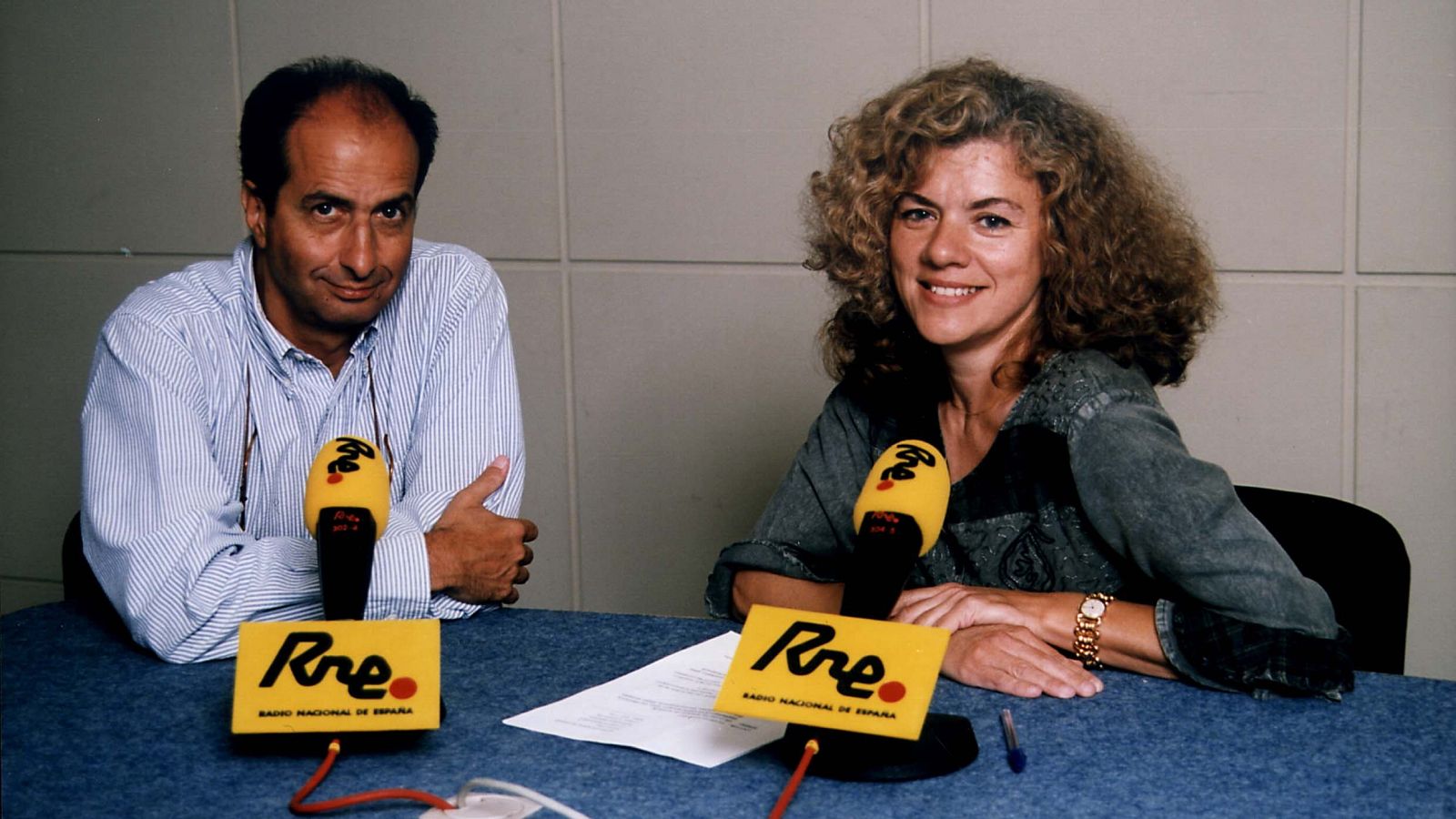 Fernando Argenta y Araceli González Campa, sentados en un estudio de radio, frente a micrófonos con el logo de RNE. En la mesa, con mantel azul, hay papeles y un bolígrafo.