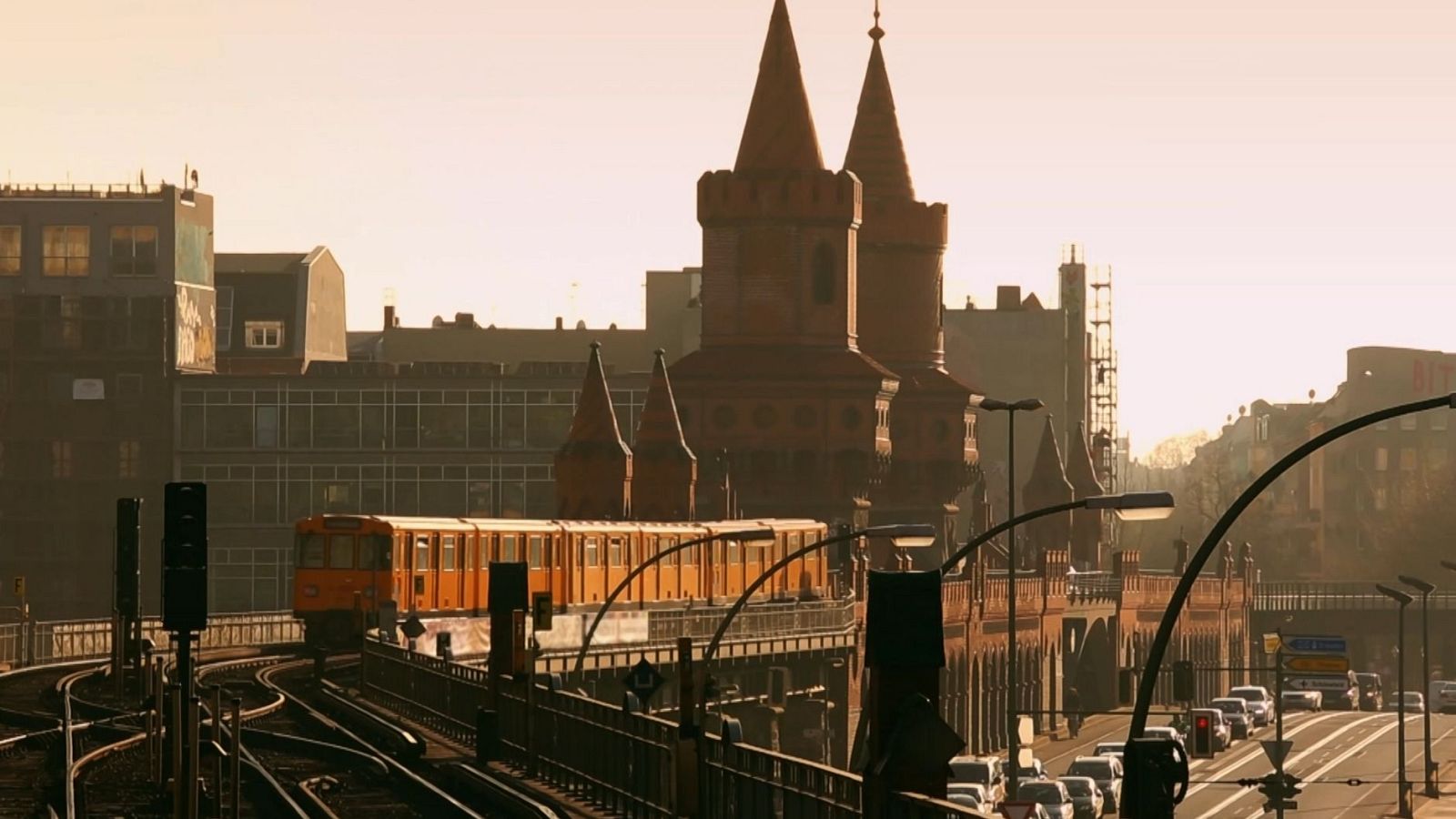 Un tren elevat taronja es mou davant de l'Oberbaumbrücke, un pont amb dues torres, a Berlín, amb trànsit a la carretera i edificis al fons.