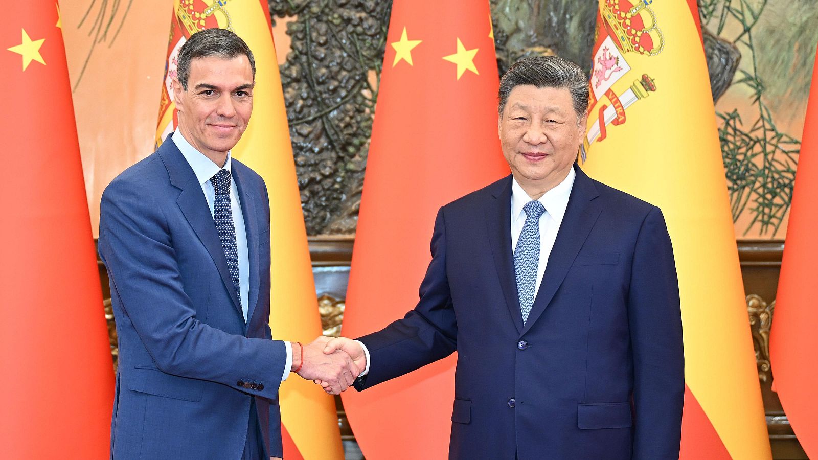 Fotografía de el presidente chino, Xi Jinping, con el presidente del Gobierno español, Pedro Sánchez, dándose la mano con banderas de China y España detrás,  en el Gran Salón del Pueblo en Pekín, capital de China