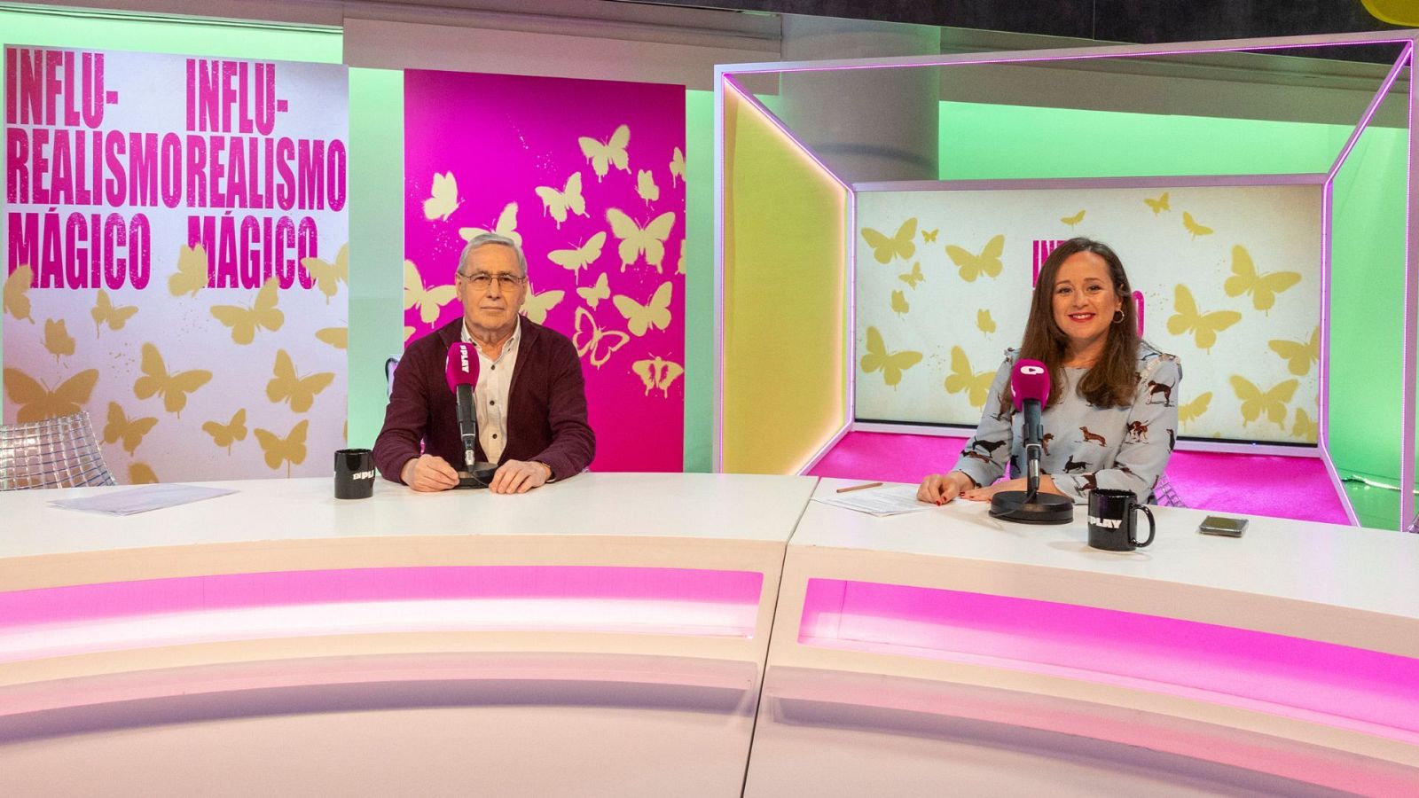 En un estudio, dos personas están sentadas frente a micrófonos. Detrás, una decoración con mariposas y fondos de colores. A la izquierda, se observa un texto repetido verticalmente.