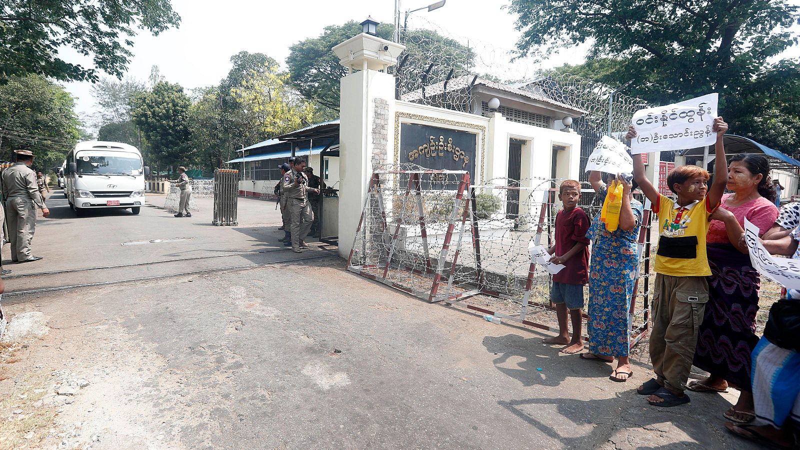 Fotografía de la puerta de la prisión de Yangon, Myanmar, en la que Familiares y amigos sostienen pancartas mientras pasan los autobuses que transportan a los reclusos liberados
