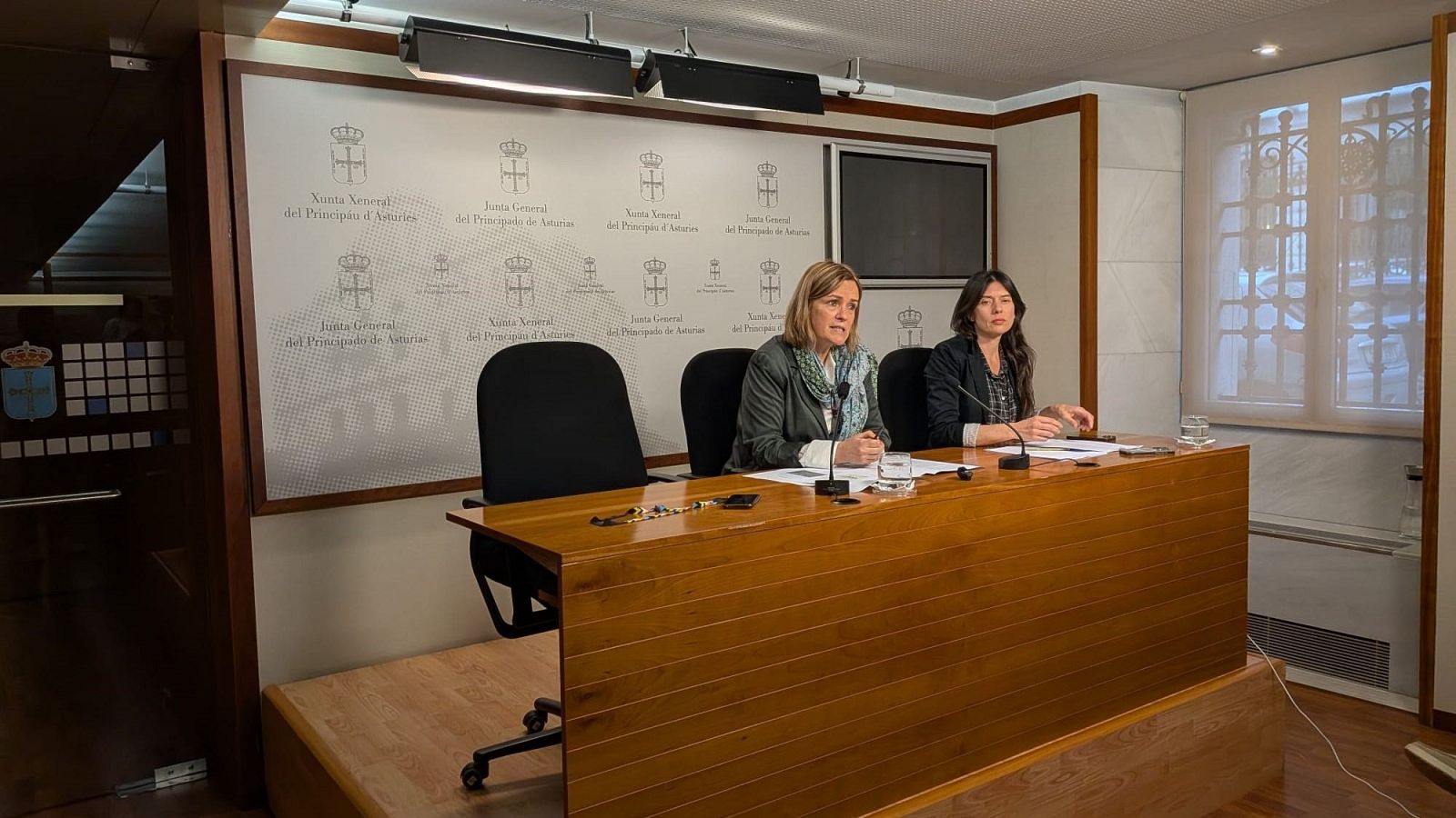 Covadonga Tomé y Laura Tuero en una rueda de prensa en la Junta General del Principado de Asturias, sentadas tras una mesa con micrófonos y documentos.