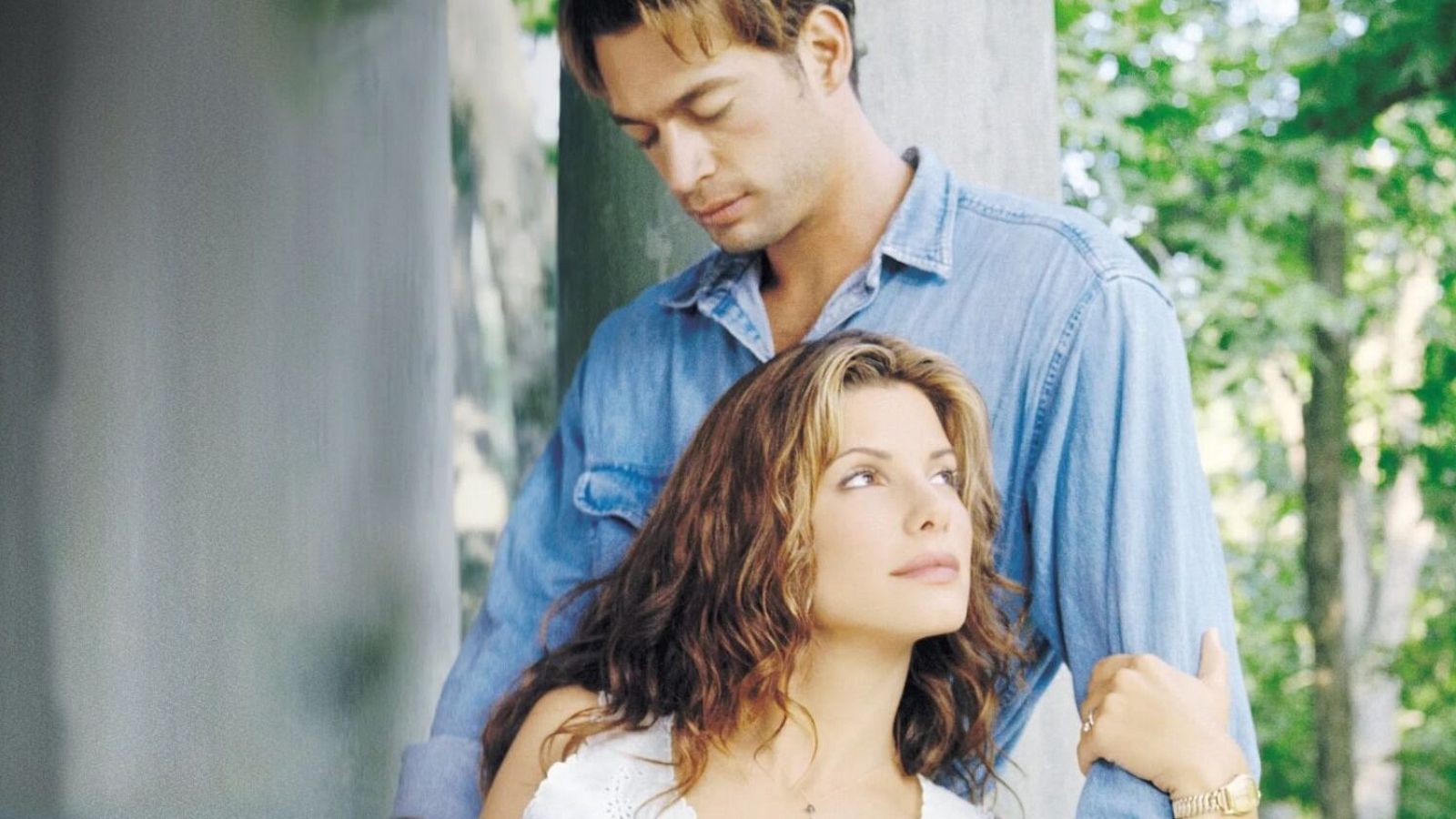 Sandra Bullock y Harry Connick Jr. comparten un momento afectuoso, ella con la mirada al cielo y él rodeándola. El fondo es natural y difuso.