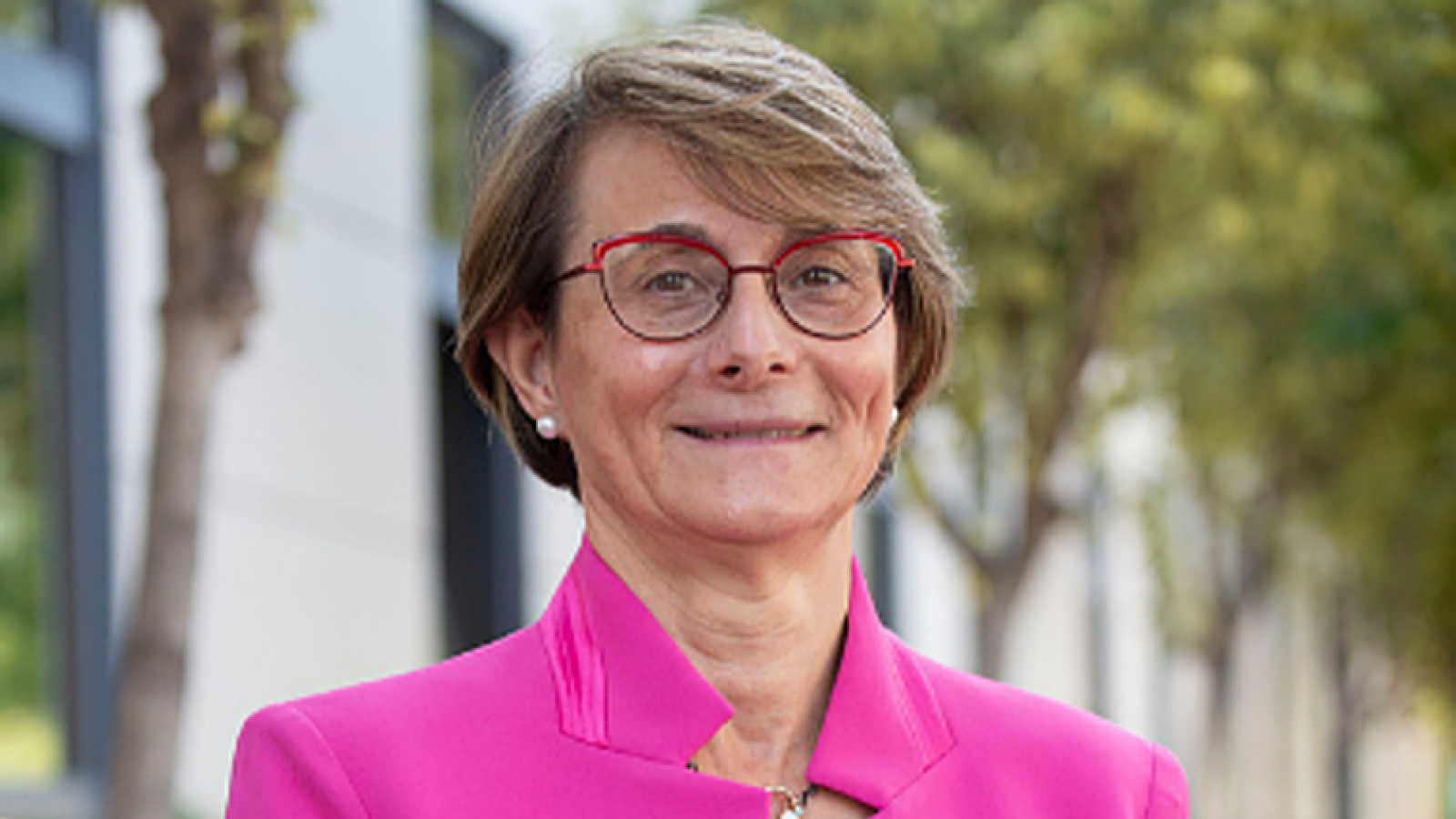 Retrato de Eva Alcón, rectora de la UJI, con gafas rojas, chaqueta fucsia y fondo verde.