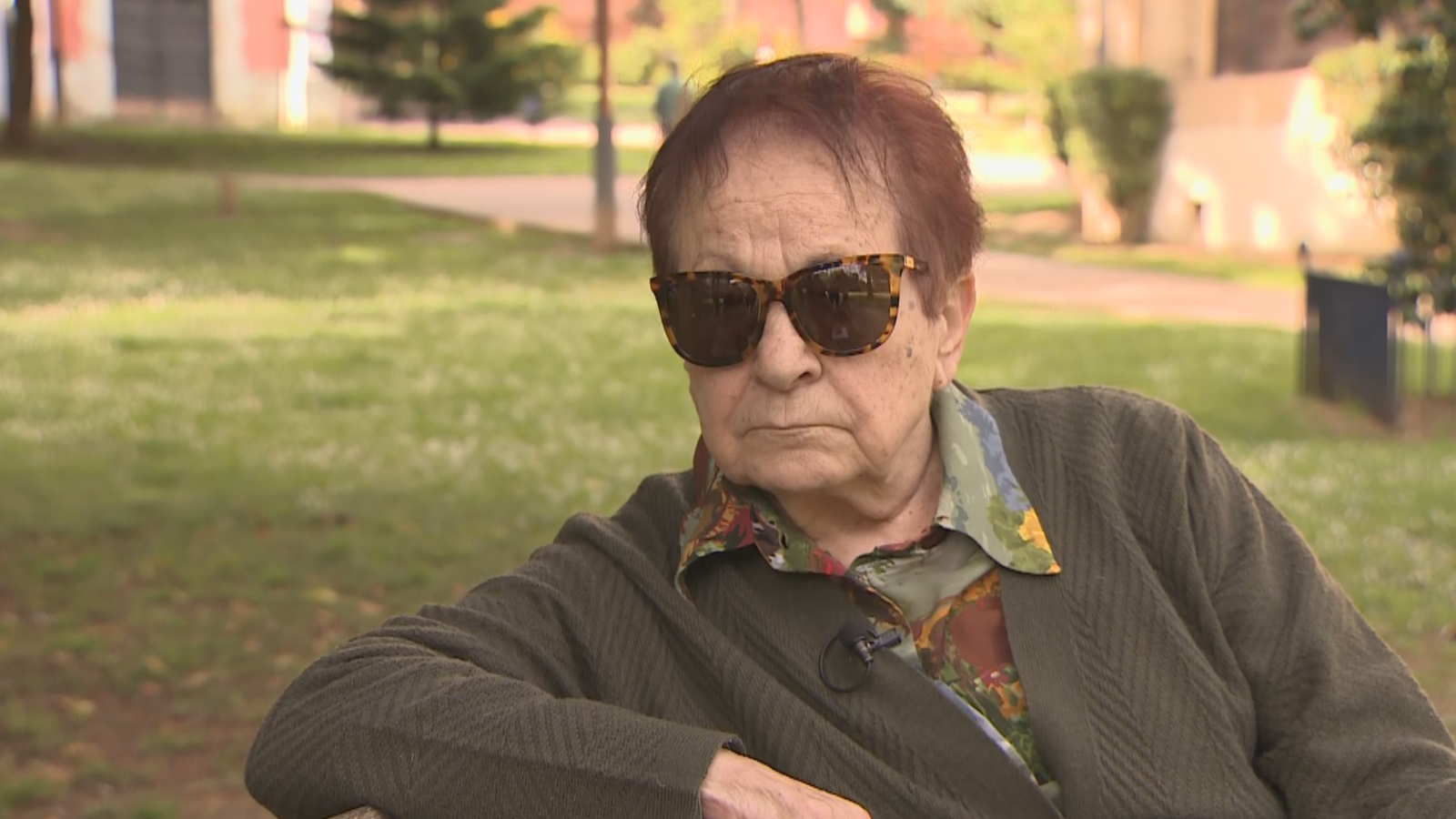 Primer plano de Esther Cabezudo, política socialista, con gafas de sol, camisa estampada y cárdigan verde, al aire libre.
