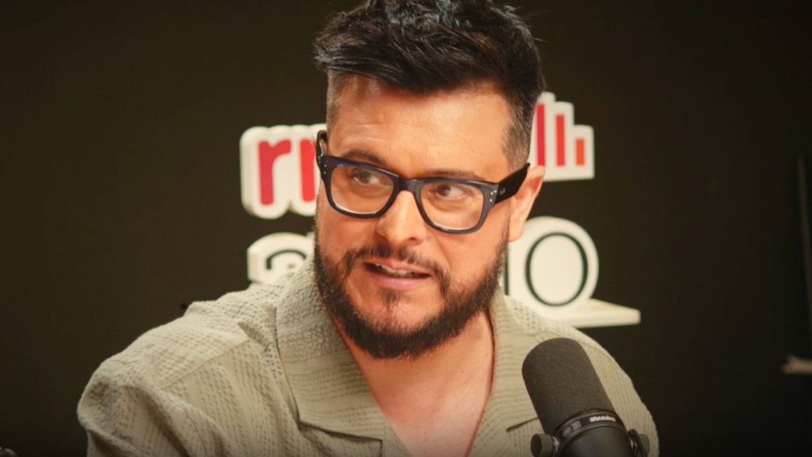 Martin Barreiro, presentador con gafas y barba, en un estudio de radio con logo y micrófono. Camisa verde oliva.