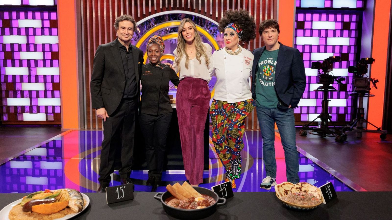 Cinco personas, incluyendo a Pepe Rodríguez Rey, Mayra Adam Chalé, La Terremoto de Alcorcón y Jordi Cruz Mas, posan en un plató de televisión con tres platos de comida y carteles de tiempo.