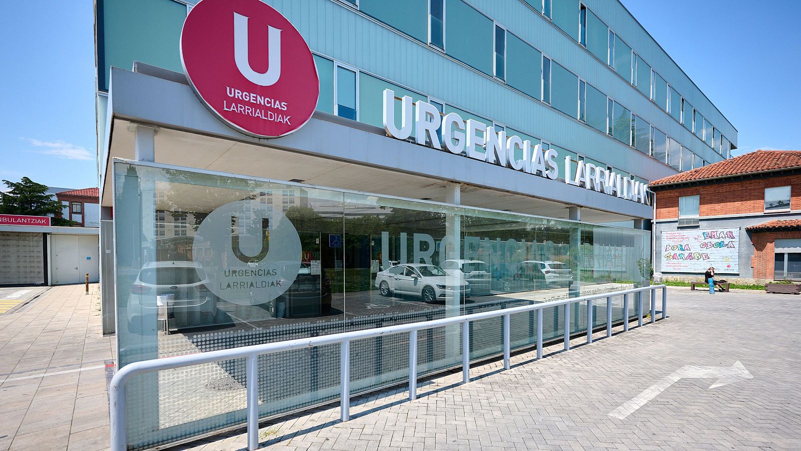 Fachada del servicio de urgencias del Hospital Universitario de Navarra, destacando el rótulo "URGENCIAS LARRIALDIAK" y la entrada acristalada.
