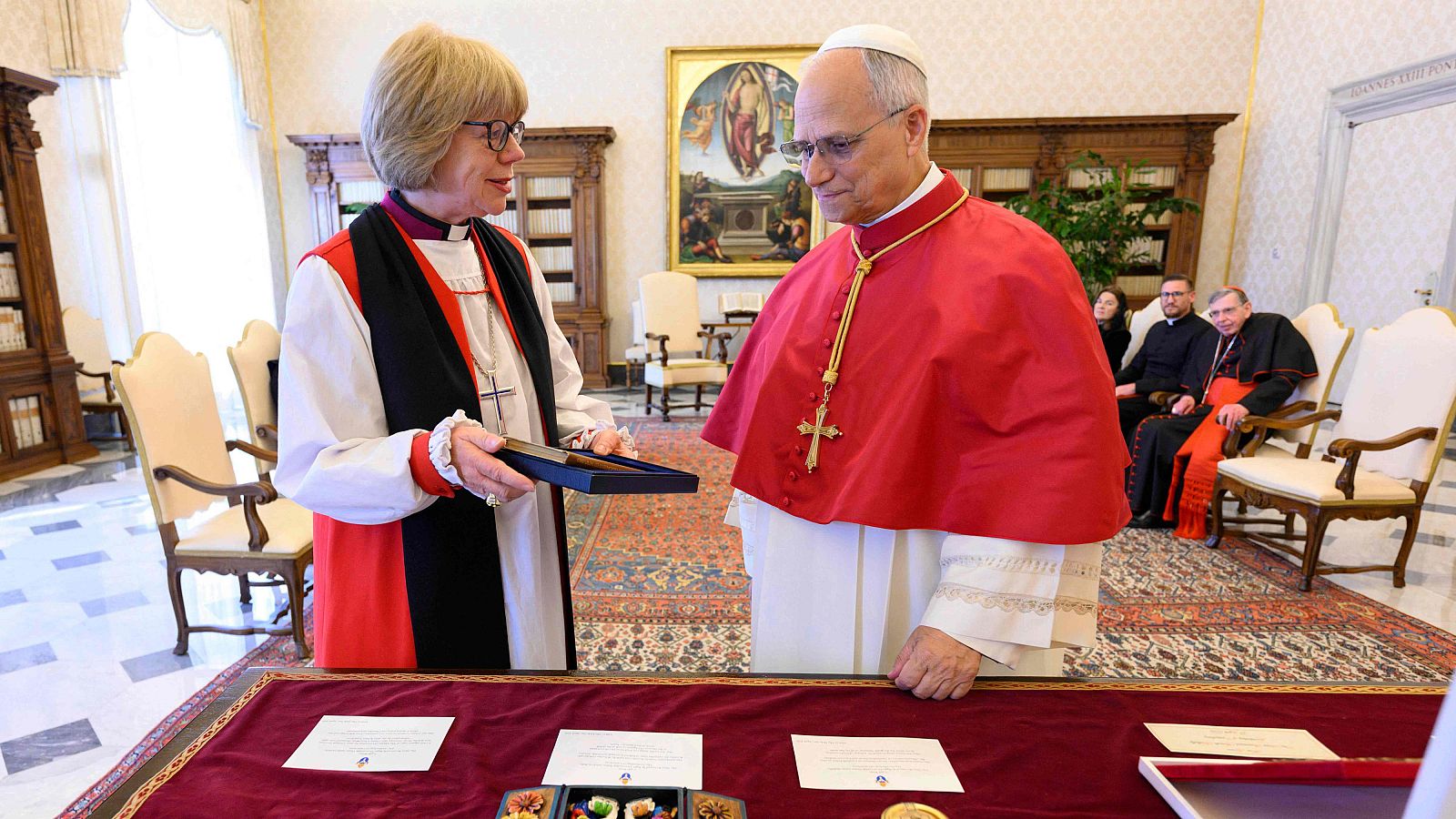 Sarah Mullally entrega un objeto al Cardenal Pietro Parolin en una sala decorada. Ambos visten atuendos clericales. Se observa una mesa con documentos y una alfombra oriental.