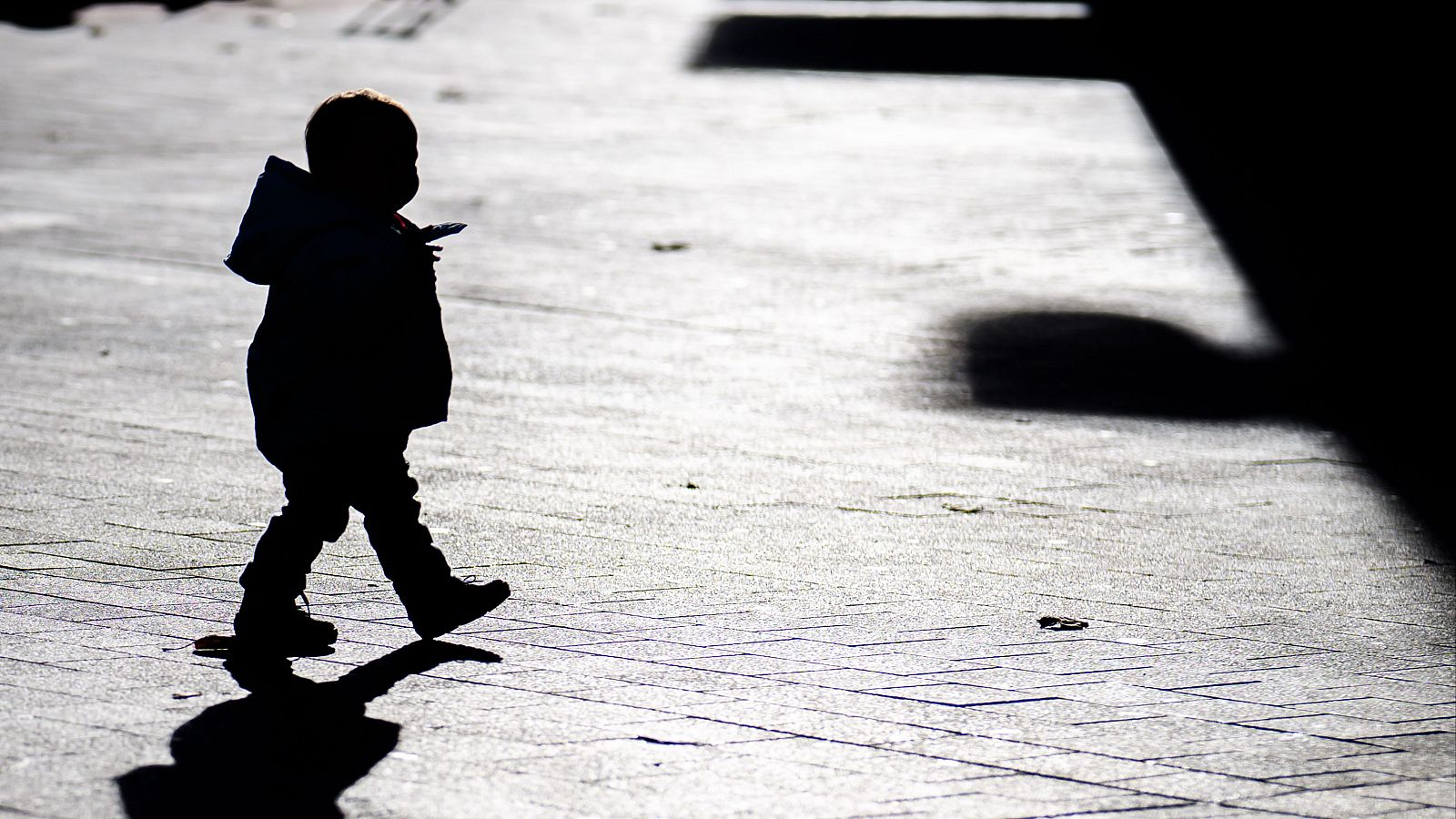 Fotografía de un niño pequeño caminando por el centro de la ciudad y proyecta una larga sombra en el suelo a contraluz.