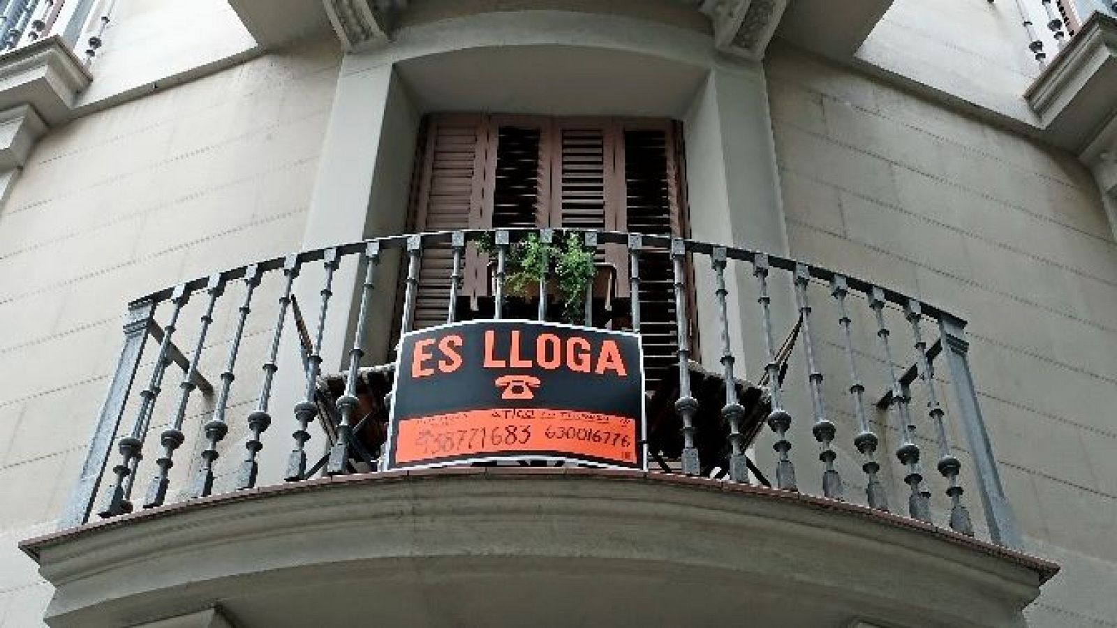 Cartel naranja y negro en balcón: "ES LLOGA", "ATICO EN TERRASSA", teléfonos 638771683 y 630016776. Balcón semicircular con barandilla de hierro forjado.