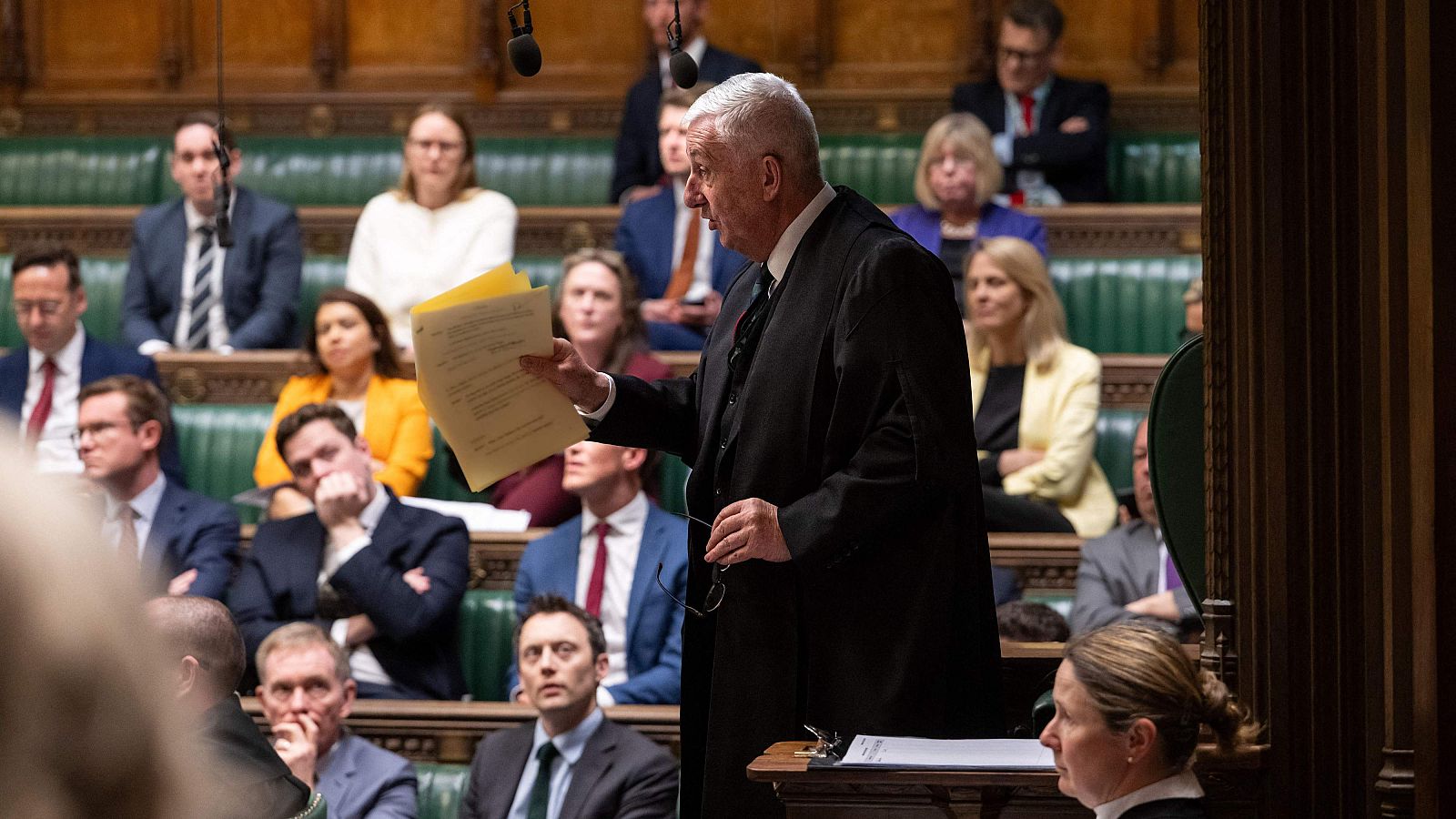 Lindsay Hoyle, presidente de la Cámara de los Comunes, preside un debate en Londres, vistiendo toga ceremonial y sosteniendo papeles, rodeado de miembros del parlamento en los bancos verdes.