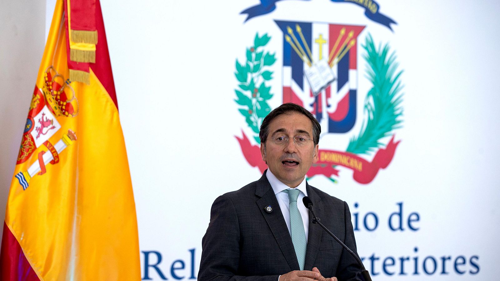 José Manuel Albares, Ministro de Asuntos Exteriores de España, habla en una rueda de prensa en Santo Domingo, con la bandera de España y el escudo dominicano de fondo.