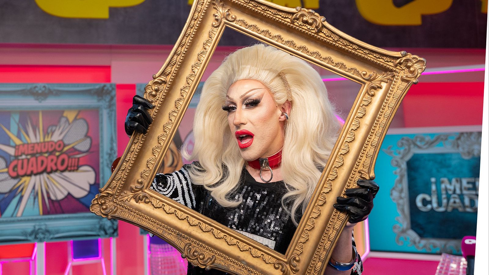 Samantha Ballantines, drag queen española, posa con un marco dorado en un set de televisión con arte pop y el texto "¡MENUDO CUADRO!!!".