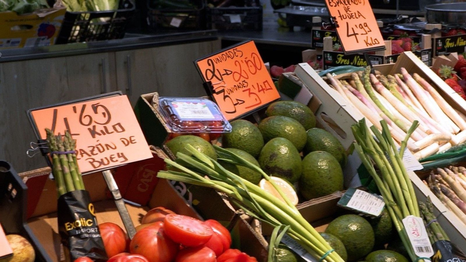 Puesto de frutas y verduras con espárragos, tomates, aguacates y frutos rojos. Precios: "1,65 KILO RAZÓN DE BUEY", "ESPARRAGO DE TUDELA 4,99 KILO", "UNIDADES 2 -> 2,50", "UNIDADES 3 -> 3,40".