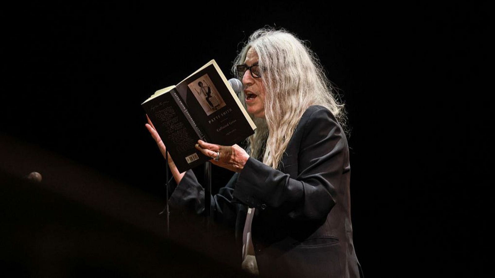 Patti Smith leyendo poemas sobre el escenario durante un concierto en Dublín en 2025