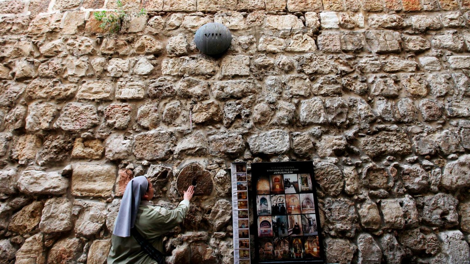 Monja tocando piedra con cruz grabada en la octava estación del Vía Crucis, Vía Dolorosa, Jerusalén.