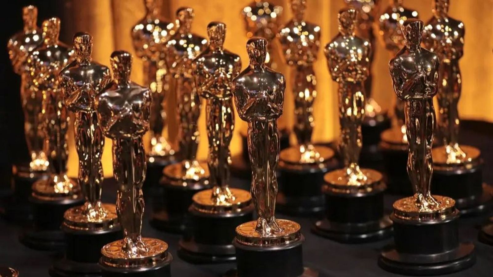 Una fotografía muestra una colección de estatuillas doradas, posiblemente premios, con figuras humanas estilizadas sobre bases oscuras, exhibidas sobre un fondo dorado.