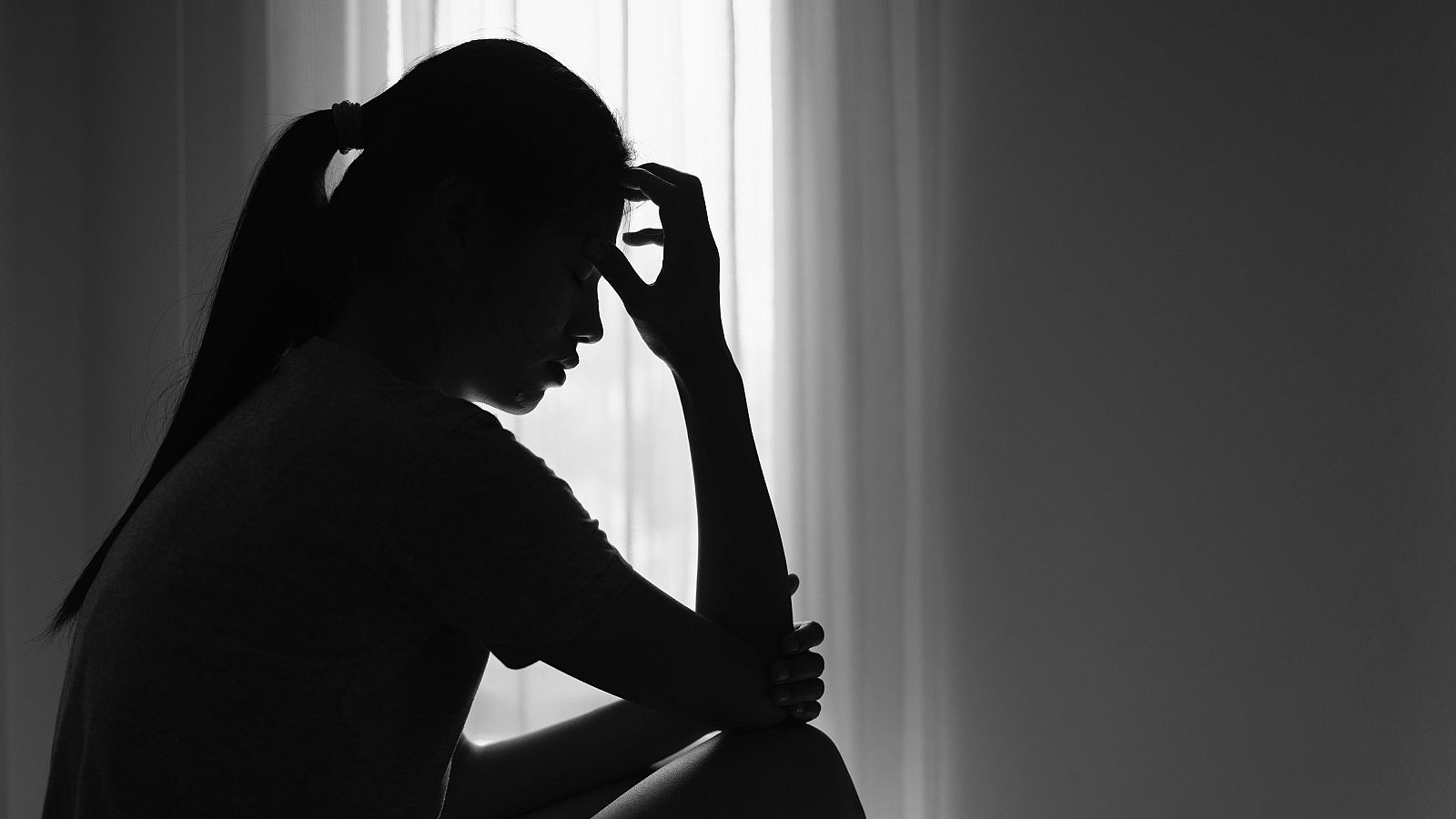 Fotografía de una mujer joven sentada en un cuarto oscuro preocupada