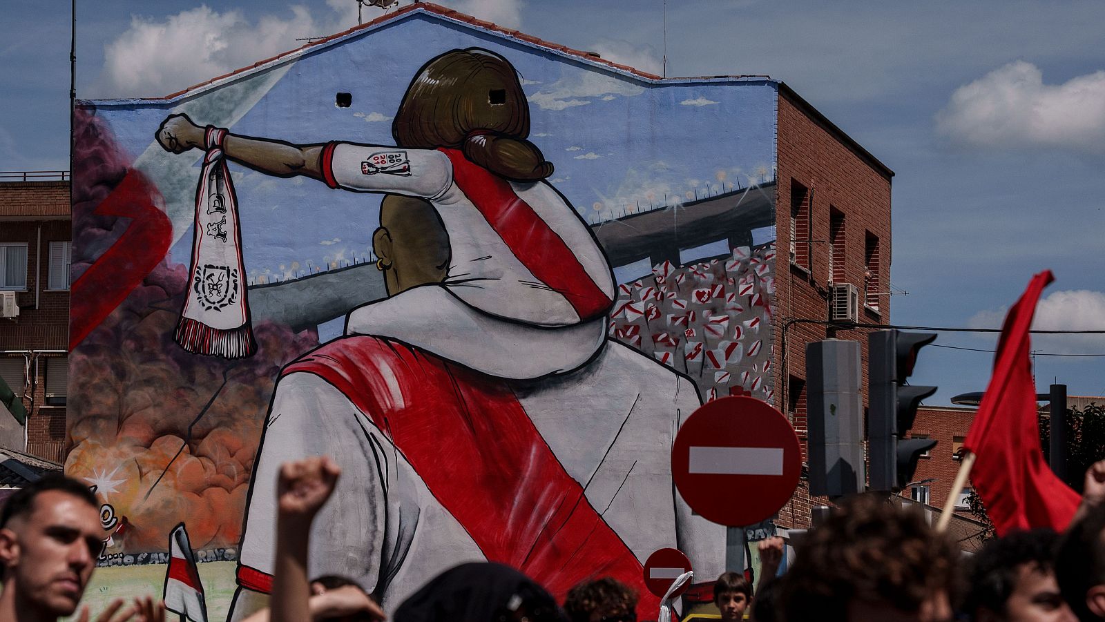 Mural artístico en un edificio de Vallecas que muestra a un padre con la camiseta del Rayo Vallecano llevando a su hija a hombros.